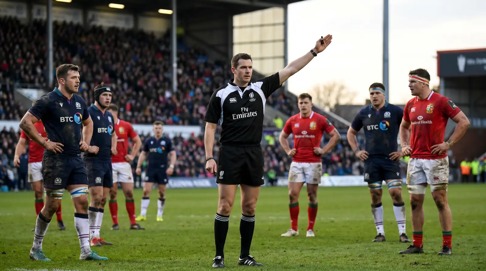 Rugby referee extending an arm to signal a penalty with players in the background