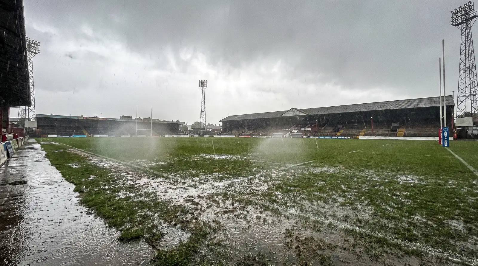Rain-soaked rugby pitch at an English ground with puddles visible on the surface